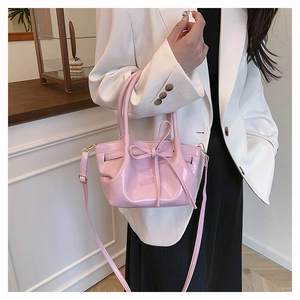 Detail of pink glossy leather handbag featuring a stylish bow and adjustable strap