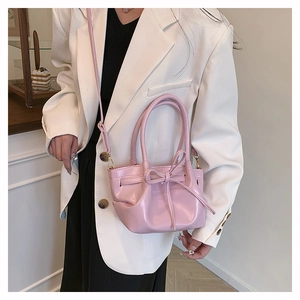 Close-up of pink glossy mini bucket bag with bow detail and adjustable cross-body strap