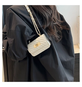 Detail of white quilted crossbody bag with gold chain strap on a black coat back
