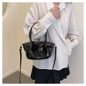 Detail of glossy black bucket bag with bow accent worn by a model in a casual outfit