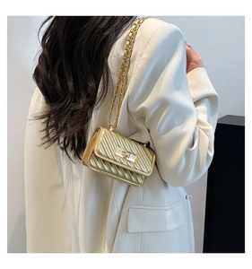 Detail of a mini gold crossbody bag with quilted texture and metal chain on white suit