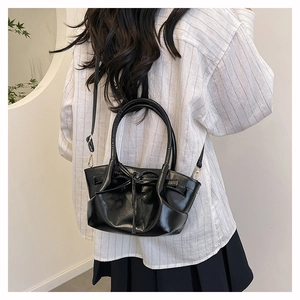 Detail of black glossy handbag with bow decoration showing the dual handles and strap