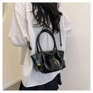 Detail of black glossy handbag with bow decoration and pleated design shown on model