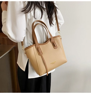 Model wearing a dual-tone tan and brown tote bag with gold logo and detachable strap