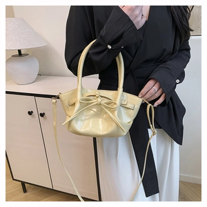Detail view of a creamy yellow glossy handbag with a large bow and shoulder strap