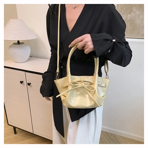 Detail of a light yellow patent leather bucket bag with a bow and elegant pleats