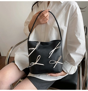 Detail of a black leather bucket bag featuring four white bows shown with a lifestyle model