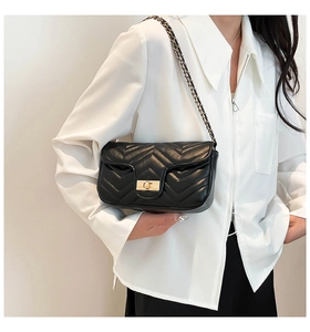 Detail view of black quilted leather crossbody bag with golden rotating metal lock and chain