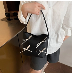 Detail der schwarzen Handtasche aus Leder mit vier beigen Schleifen und schmalem Riemen