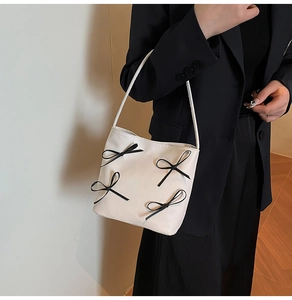 Close-up of a white hobo bag with black bows worn on the shoulder of a black blazer