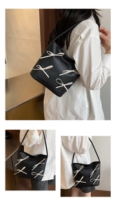 Detail of black leather shoulder bucket bag featuring decorative cream bow accents