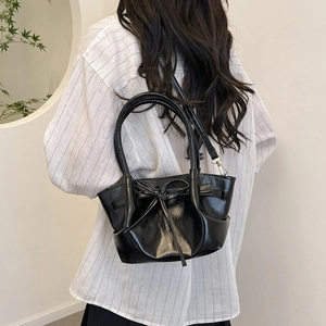 Glossy black patent leather bucket bag with bow detail worn by model in minimalist setting