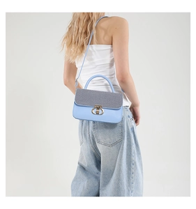 Detail of light blue handbag with grey woven flap and gold T-shaped clasp on a model