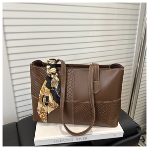 Detail of brown patchwork leather tote bag with embossed textures and a decorative silk scarf