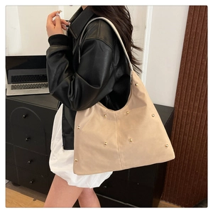 Detail of hobo shoulder bag with gold studs on matte beige material in office setting