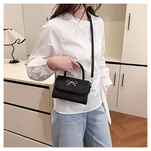 Detail of black glitter crossbody bag with silver bow accent on model in room