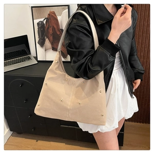 Detailed view of beige hobo bag with gold stud accents worn by a model in a modern office