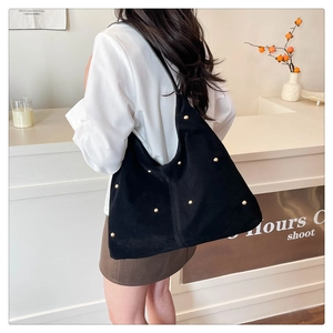 Détail du grand sac cabas noir mat avec clous dorés porté à l'épaule par un mannequin