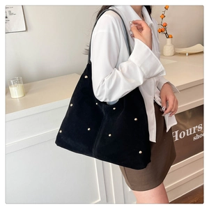 Detail of black suede tote bag with golden studs worn by model in a bright room