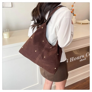 Detail of dark brown suede shoulder bag with golden rivets worn by model in a cafe