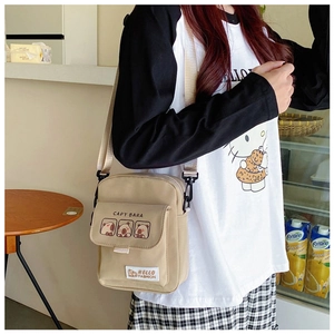 Detail of khaki canvas crossbody bag featuring cute cartoon capybara print and textile label