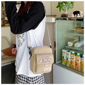 Detail view of beige canvas crossbody bag featuring three cartoon capybaras on front flap