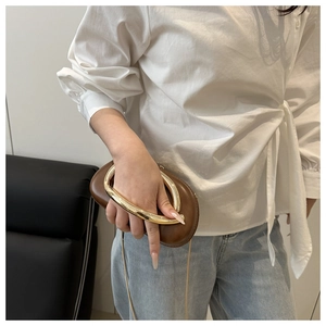 Detailed shot of brown PU leather clutch with curved gold metal handle and chain strap