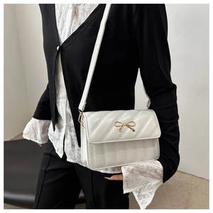 Model showing white crossbody bag with gold bow detail and V-shaped quilted texture