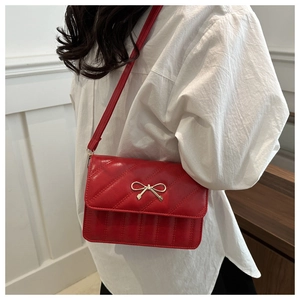 Détail du sac à bandoulière rouge matelassé avec nœud doré porté par un mannequin à l'intérieur