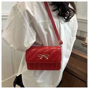 Detail of red quilted crossbody bag featuring a golden bow buckle and leather strap