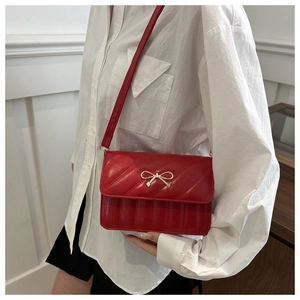 Close-up of red crossbody bag featuring quilted patterns and a golden bow decoration