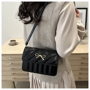 Detail of black quilted crossbody bag with golden bow metallic accent and slim strap