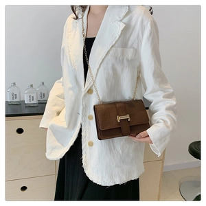 Detail of dark brown stone pattern crossbody bag with gold H buckle on white blazer