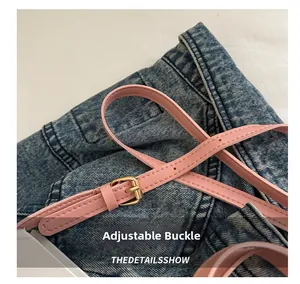 Détail de la ceinture en cuir rose avec boucle en métal doré sur fond en denim bleu
