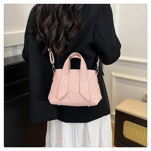 Detail of light pink tote bag with textured leather, decorative straps and metal studs