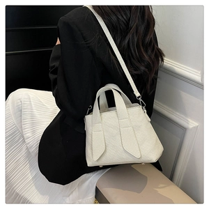 Detail view of cream tote bag with textured surface and metallic bottom rivets on model