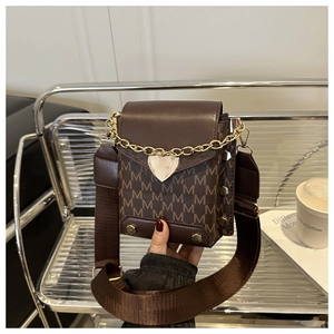 Detail of retro dark brown mini square bag with M-pattern and gold heart pendant