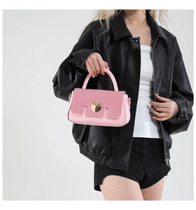 Sac à main en cuir rose avec boucle dorée porté par un mannequin en veste de cuir noire