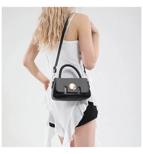 Détail d'un sac à bandoulière en cuir noir avec un fermoir métallique doré circulaire