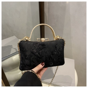 Detail of black lace evening clutch featuring golden butterfly clasp and metal handle