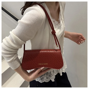 Detail of red crocodile texture baguette bag with gold lettering on a white lace outfit