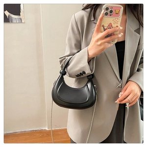 Chic black crescent bag with knotted handle and metal chain shown on gray blazer