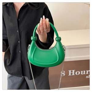 Close-up of green crescent bag with cylindrical handle and circular embossed detail