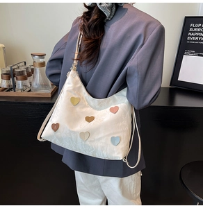 Detail shot of a cream white nylon shoulder bag featuring colorful heart-shaped patches