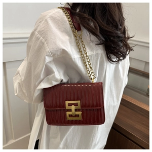 Detail of burgundy quilted shoulder bag featuring gold chain strap and geometric metal clasp