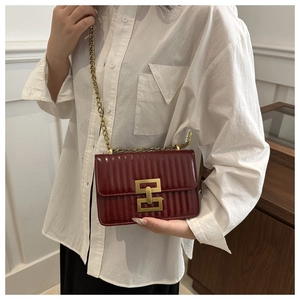 Detail of burgundy shoulder bag with gold chain strap and square metal buckle on a model