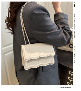 Close-up of cream textured leather shoulder bag with wavy flap and chain strap