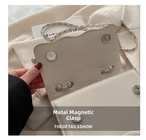 Detail view of dual silver magnetic buckles on a beige lychee grain leather chain bag