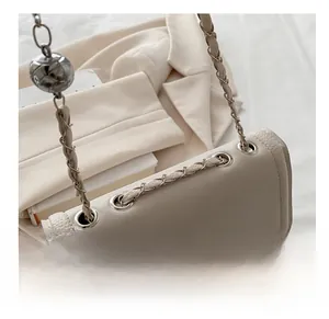 Detail of silver grommets and woven chain strap on a beige pebbled leather shoulder bag