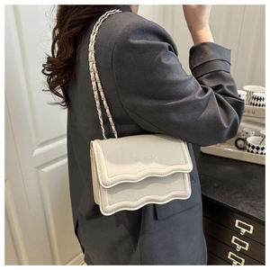 Detail of off-white crossbody bag with wavy flap design and woven chain strap on model